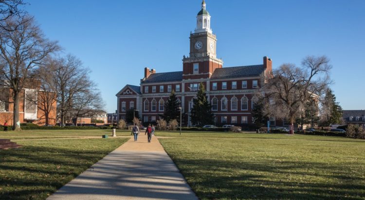 Library at Howard University with three students walking on pathway towards library, library is surrounded by green grass and trees